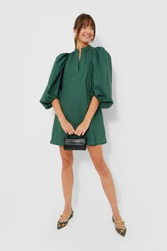 a woman in a green dress is holding a black purse and posing for the camera