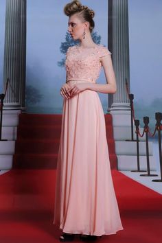 a woman in a long pink dress standing on a red carpet with columns behind her