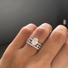 a woman's hand with two wedding rings on her left and the other hand holding an engagement ring