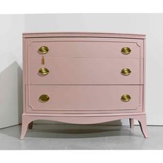 a pink chest of drawers with brass handles and knobs on the top, against a white wall