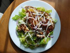 a white plate topped with lettuce and meat on top of a wooden table