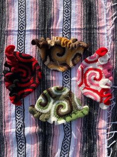 four crocheted hats laying on top of a striped blanket