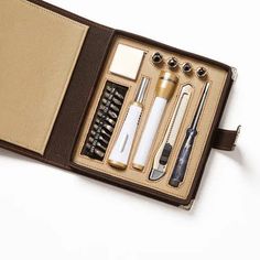 an open leather case with pens, scissors and other items in it on a white surface