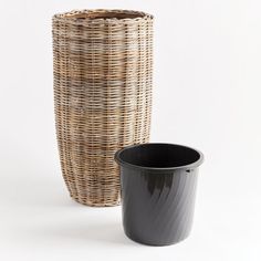 a black cup sitting next to a wicker basket on a white background with the lid off