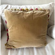 a brown pillow with pom poms on it sitting on a white couch next to pillows