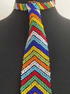 👔 Absolutely stunning beaded tie, handmade by highly skilled Zulu women in Kwa-Zulu Natal, South Africa. 👔 This gorgeous tie is made up of thousands of glass beads, each one threaded by hand to make an absolutely beautiful tie in a colourful chevron design. 👔 The tie is fastened with a single beaded loop and ball clasp and lies flat on the chest. 👔 Remarkable beadwork - exceptionally high quality and real showstopper.  If you're looking to make a statement, this tie is for you! 👔 Neck measurement 35cm (14in). Length 29cm.  Width 5.5cm 👔 See my other listings for alternative sizes and colours. More about us.... Our products are all hand-made, by artists and crafters in South Africa. We source suppliers with the highest quality standards. Where possible, we show images of the exact pro Bohemian Beaded Bracelets With Colorful Beads For Weddings, Bohemian Multicolor Beaded Necklaces For Wedding, Multicolor Large Beads For Wedding, Bohemian Multicolor Beaded Necklace For Wedding, Bohemian Multicolor Beaded Bracelets For Weddings, Bohemian Tiny Beads For Wedding, Bohemian Multicolor Wedding Beads, Traditional Adjustable Beads For Party, Adjustable Multicolor Beaded Bracelets For Wedding