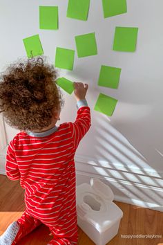 a young child is playing with post - it notes on the wall in front of her