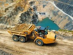 a yellow dump truck driving down a dirt road next to a large body of water