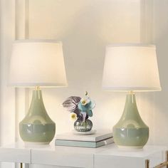 two green vases sitting on top of a table next to each other with white lamps