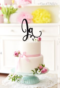 a white cake with pink flowers and a monogrammed letter on top is sitting on a table