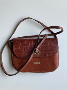 "♥ Vintage 80s-90s cute crossbody bag, 1 compartment. ♥ Stylish and luxury looking rich brown color with embossed reptile texture details & signature metal badge on the front. ♥ Twist lock fastener on the front flap with El Campero lettering around it.  ♥ At least partially genuine leather. ♥ Adjustable buckle strap. ♥ Good vintage condition, there are some leather scratches and other minor signs of wear.  ♥ Brand: EL CAMPERO, an Italian brand started back in the 1960s by Giuliano Bassini (campe Retro Brown Crossbody Bag, Vintage Brown Retro Crossbody Shoulder Bag, Retro Vintage Brown Crossbody Shoulder Bag, Retro Brown Satchel With Adjustable Strap, Retro Brown Satchel For Everyday Use, Retro Saddle Bag With Detachable Strap, Retro Vintage Brown Shoulder Bag For Everyday, Retro Saddle Bag With Adjustable Strap, Retro Cognac Shoulder Bag For Daily Use