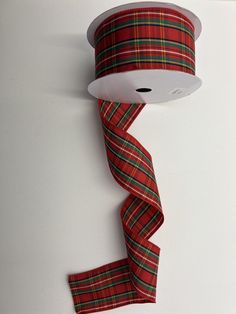 a roll of red and green plaid ribbon on a white surface with a hole in the middle