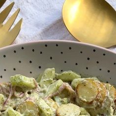 a white bowl filled with food next to gold spoons and utensils on top of a table