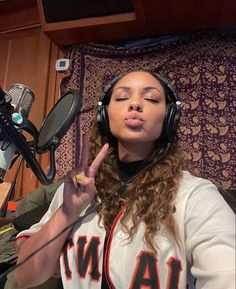 a woman with headphones on making a peace sign in front of a radio microphone