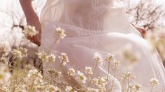 a woman in a white dress is standing among flowers