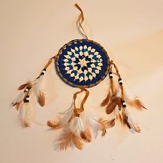 a blue and white dream catcher with feathers hanging from it's side on a wall