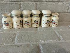 five ceramic jars are lined up against a brick wall