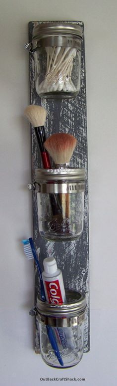 three glass jars with brushes and toothbrushes in them hanging from a metal rack