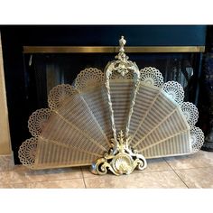 an ornately designed fan sitting on the floor in front of a fireplace mantel