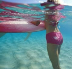 a woman in pink swimsuit holding a surfboard under water