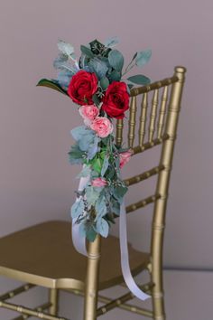 a gold chair with flowers and greenery tied to the back of it's seat