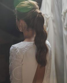 the back of a woman's head with long hair in a ponytail, wearing a white dress