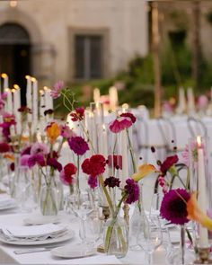 the table is set with many vases filled with flowers, candles and napkins