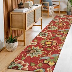 a red floral rug in the middle of a living room with wooden furniture and potted plants