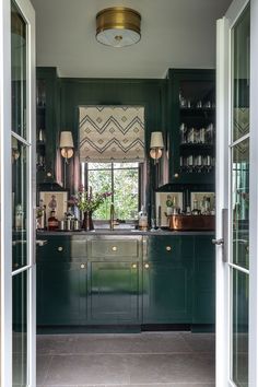 an open door leading to a kitchen with dark green cabinets and gold trimmings