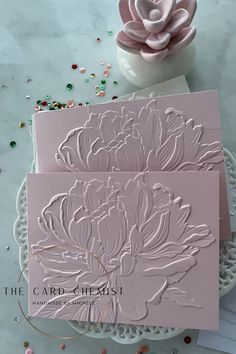 the card - chemst flower embossed on pink cards are next to a white vase with flowers in it