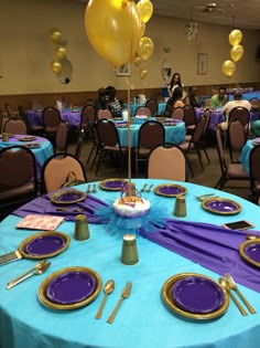 a blue table topped with purple and gold plates covered in cake next to yellow balloons