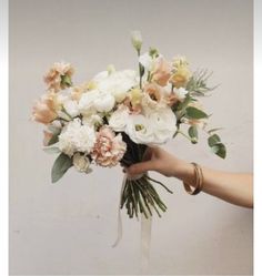 a person holding a bouquet of white and peach flowers with greenery on the stems