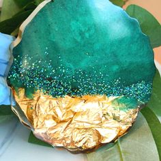 a green and gold plate sitting on top of a leafy tablecloth next to blue napkins