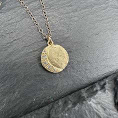 A 14k yellow gold disc mimics the full moon, with a crescent accented by tiny diamonds. This organically shaped and textured pendant rests along a 16" gold chain. Handmade in California. Diamond Half Moon Phase Necklace, Moon Phase Coin Necklace With Round Pendant, Gold Hammered Half Moon Jewelry, Hammered Gold Half Moon Jewelry, Hand Forged Moon Shaped Gold Jewelry, Hand Forged Moon-shaped Gold Jewelry, Diamond Moon Charm Necklace With Round Pendant, Crescent Moon Charm Diamond Necklace For Gift, Crescent Yellow Gold Jewelry With Rose Cut Diamonds