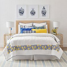 a white bed with yellow and blue pillows in a room next to two pictures on the wall