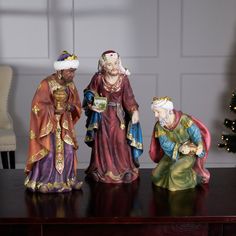 three figurines sitting on top of a wooden table next to a christmas tree