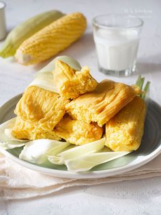 corn on the cob and other foods are sitting on a plate next to a glass of milk