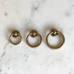 three brass rings on a marble counter top with one ring in the middle and two circles at the end