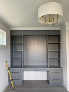 an empty room with built - in desk and shelves under a chandelier hanging from the ceiling