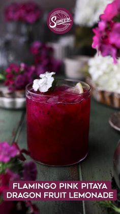 a purple drink sitting on top of a wooden table next to pink and white flowers