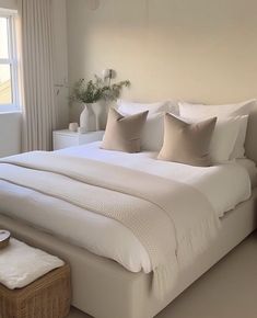 a large white bed sitting in a bedroom next to a window with lots of pillows on top of it