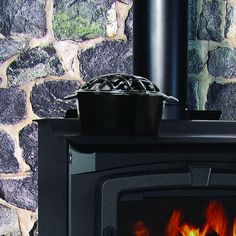 a black stove with a pot on top of it next to a stone wall and fireplace