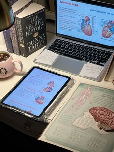 an open laptop computer sitting on top of a desk next to a book and cup