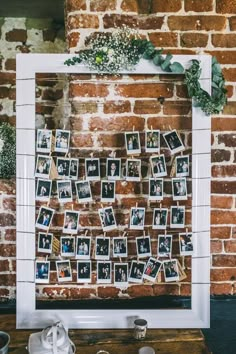 a white frame with pictures hanging on it next to coffee cups and other items in front of a brick wall