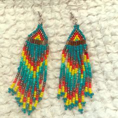 two pairs of colorful beaded earrings sitting on top of a white cloth covered table