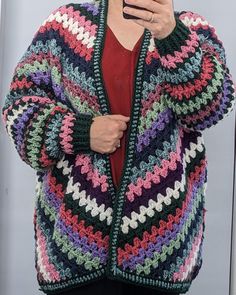 a woman is taking a selfie with her cell phone while wearing a colorful crocheted cardigan