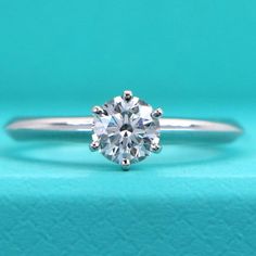 an engagement ring with a round brilliant diamond in the center on a blue background,