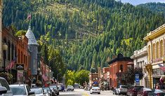 cars are parked on the street in front of some buildings and trees with mountains in the background