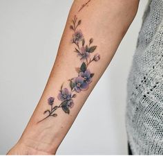 a woman's arm with purple flowers on the left side of her wrist and an arrow in the middle