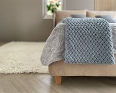 a bed with a blue blanket on top of it next to a white rug and window